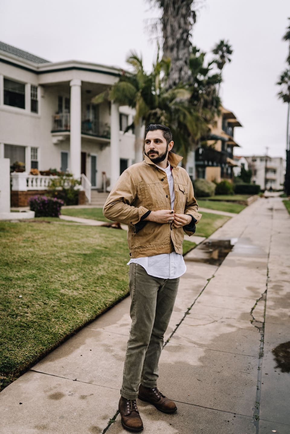 Utility workwear: A stylish man buttoning his jacket on a residential street with lush greenery.