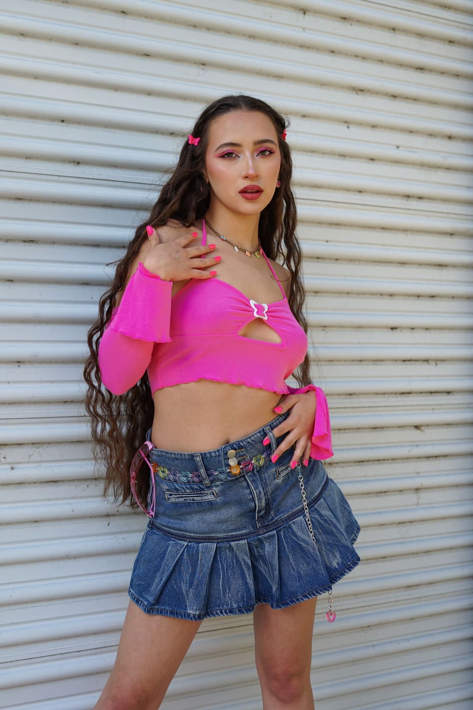 Y2K revival: Young woman posing in a vibrant Y2K style outfit with a pink crop top and denim skirt.