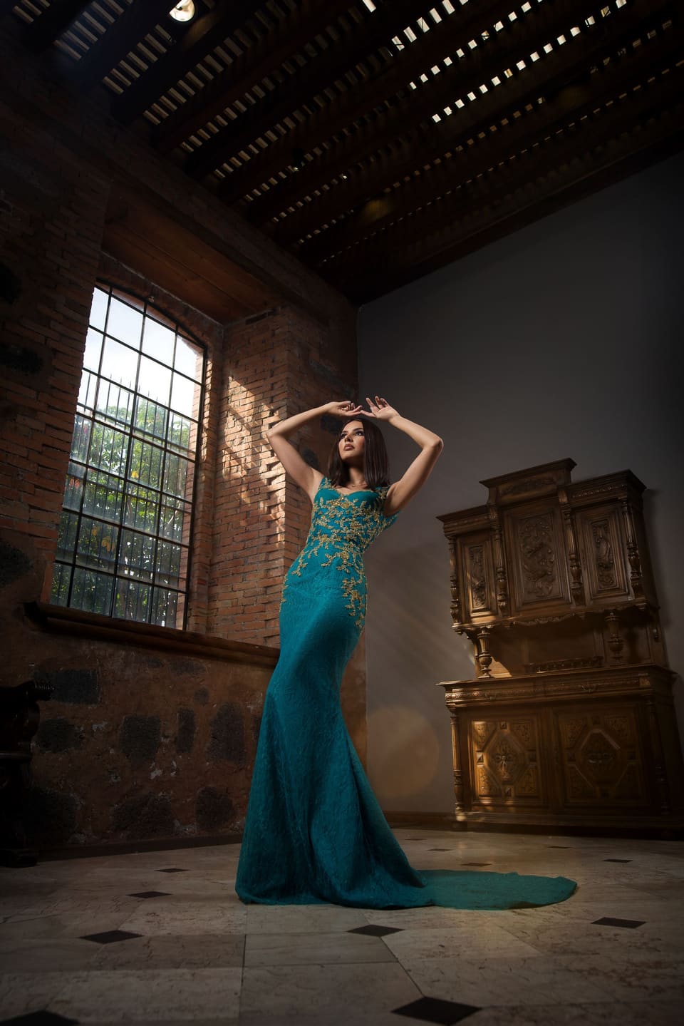 Evening glamour: Stunning fashion portrait of a woman in a blue dress posing in an ornate vintage interior setting.