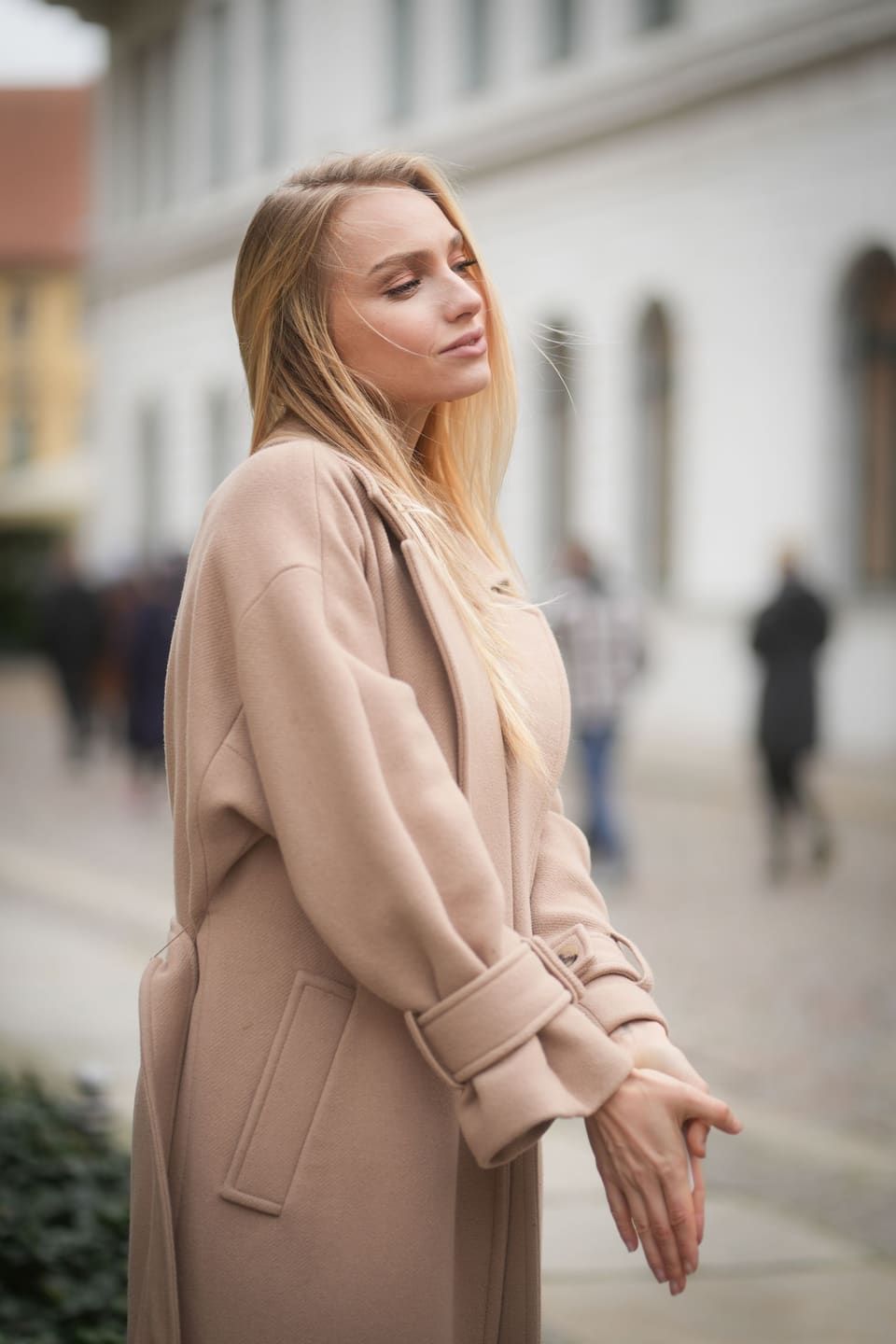 Quiet luxury: Blonde woman in a beige coat poses gracefully on an urban street in fall.