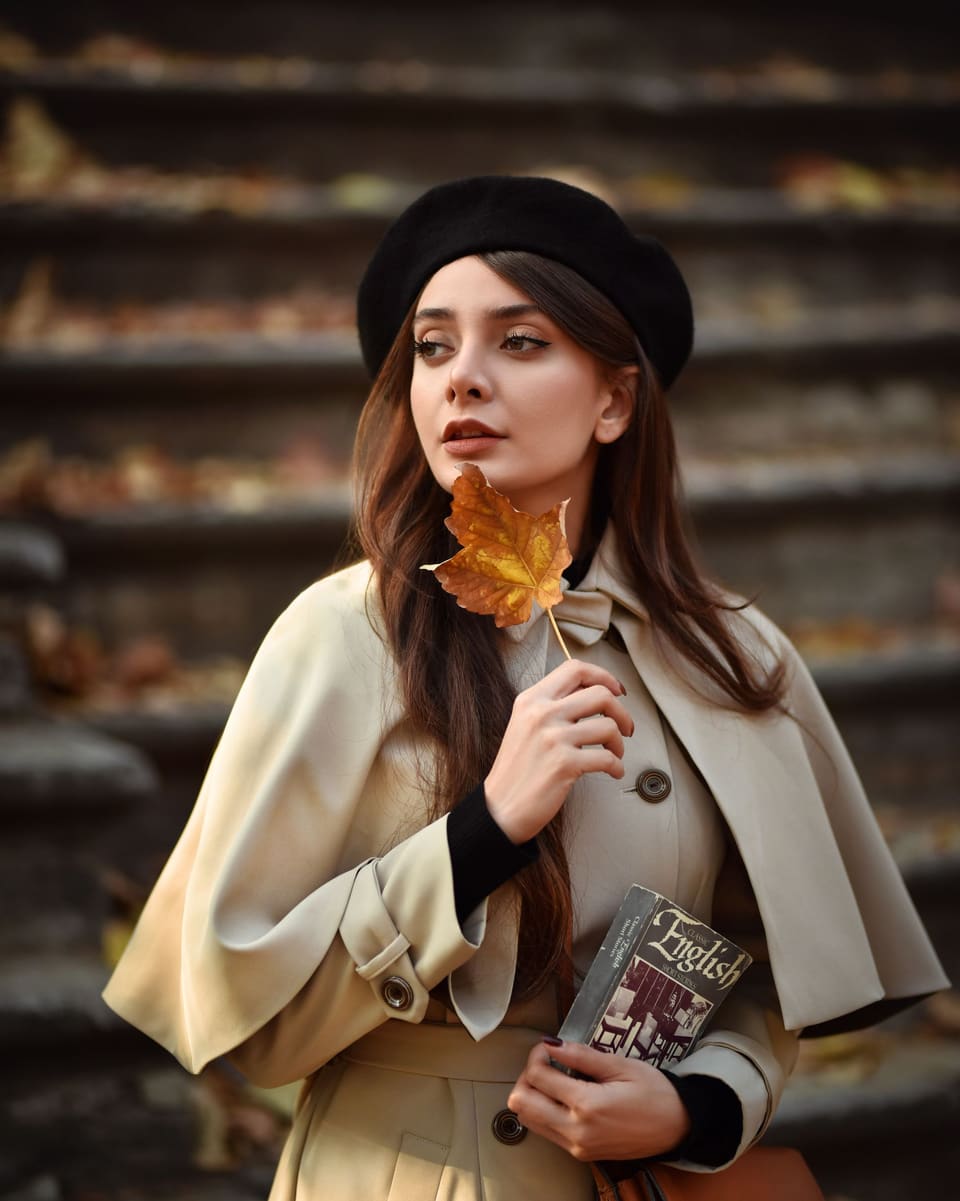 Dark academia: Elegant woman in autumn fashion holding a leaf, posing on outdoor stairs.