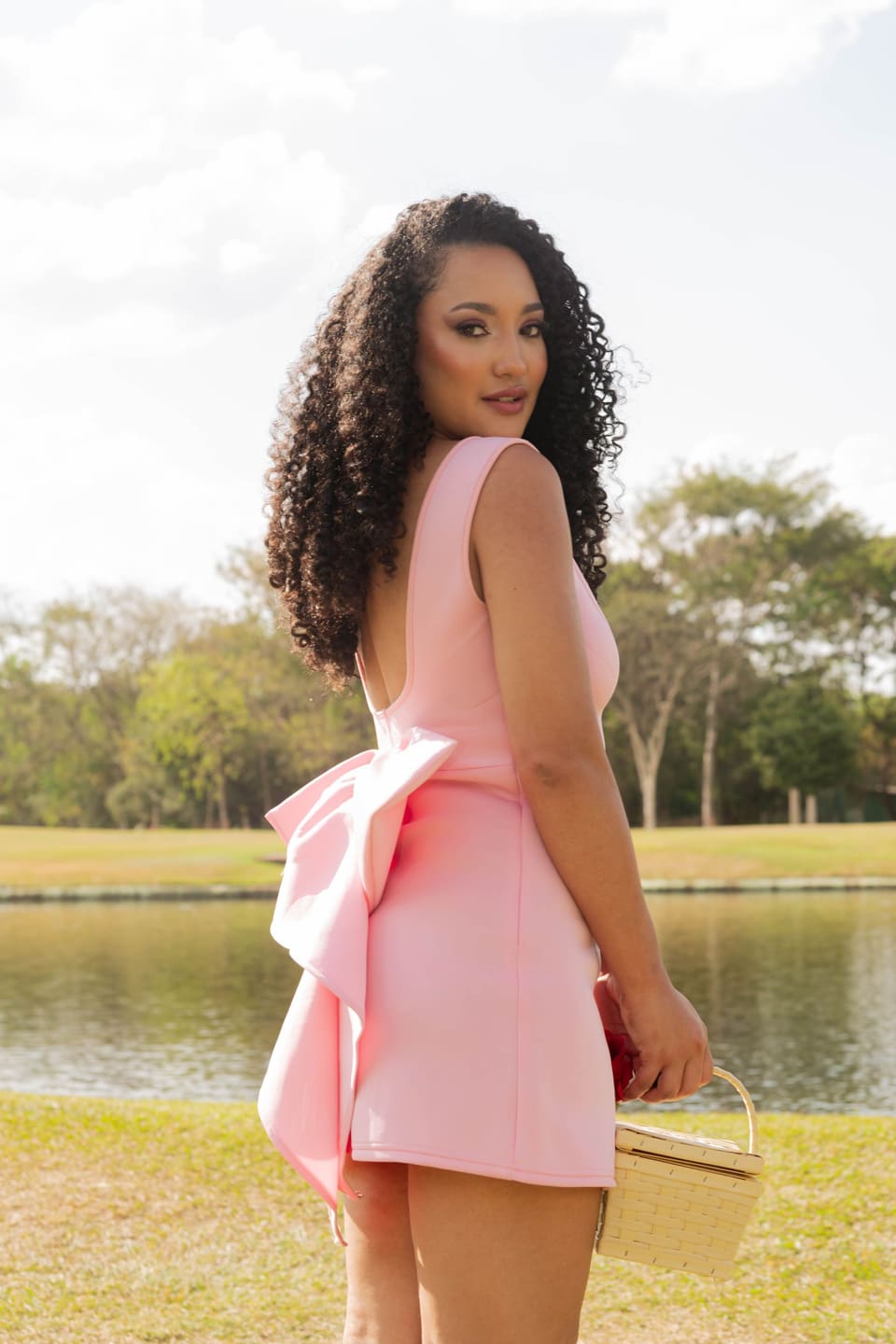 Balletcore: Stylish woman in a pink dress with a bow enjoys a sunny day by the lake.
