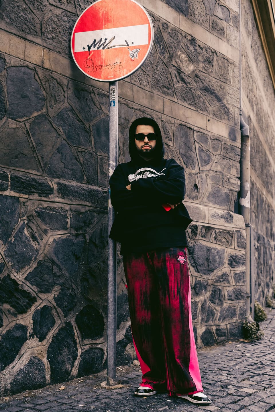 Streetwear: Stylish man in front of graffiti sign on urban street, showcasing bold streetwear fashion.
