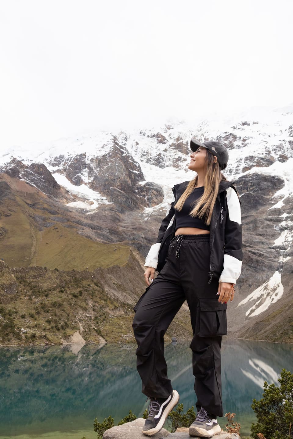 Gorpcore: A woman stands confidently by a lake in the stunning mountain scenery of Cuzco, Peru.