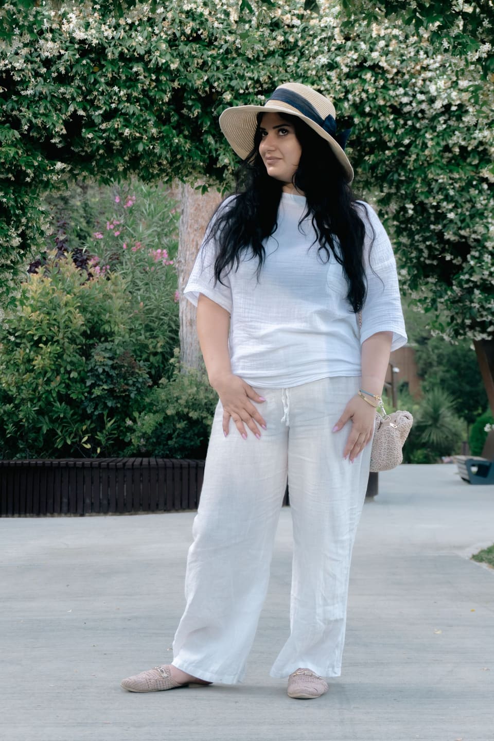 Riviera linen: Stylish woman in a white outfit and hat enjoying a sunny day in a park in Baku, Azerbaijan.