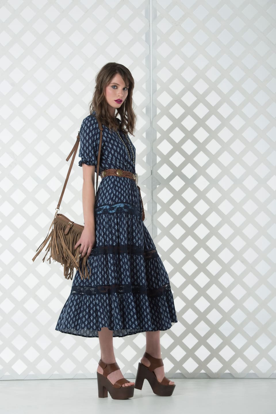 Seventies boho: Stylish woman in blue bohemian dress and fringe bag posing in front of a lattice wall.