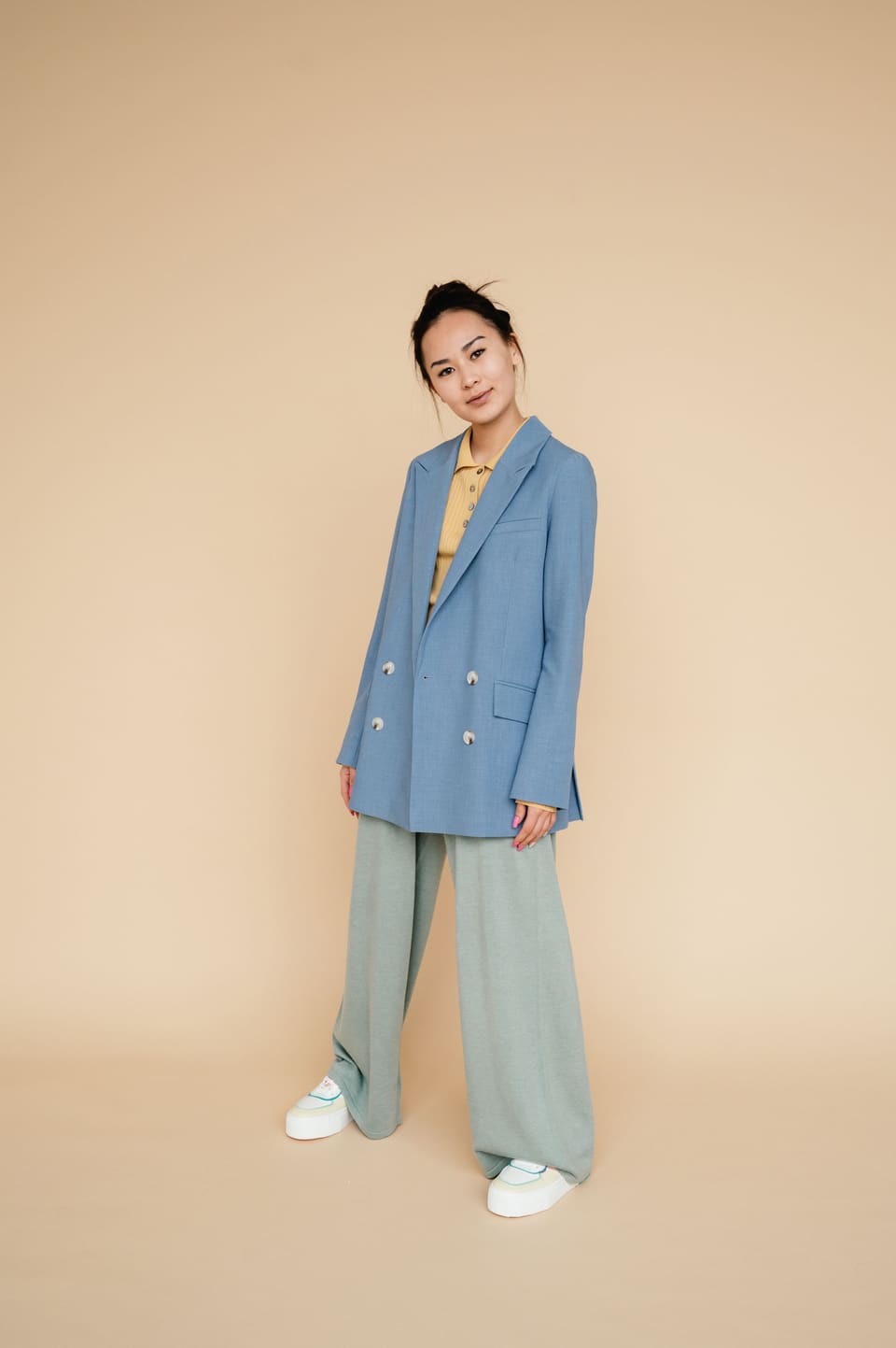Soft tailoring: Stylish woman in a blue suit and baggy pants on a yellow background.