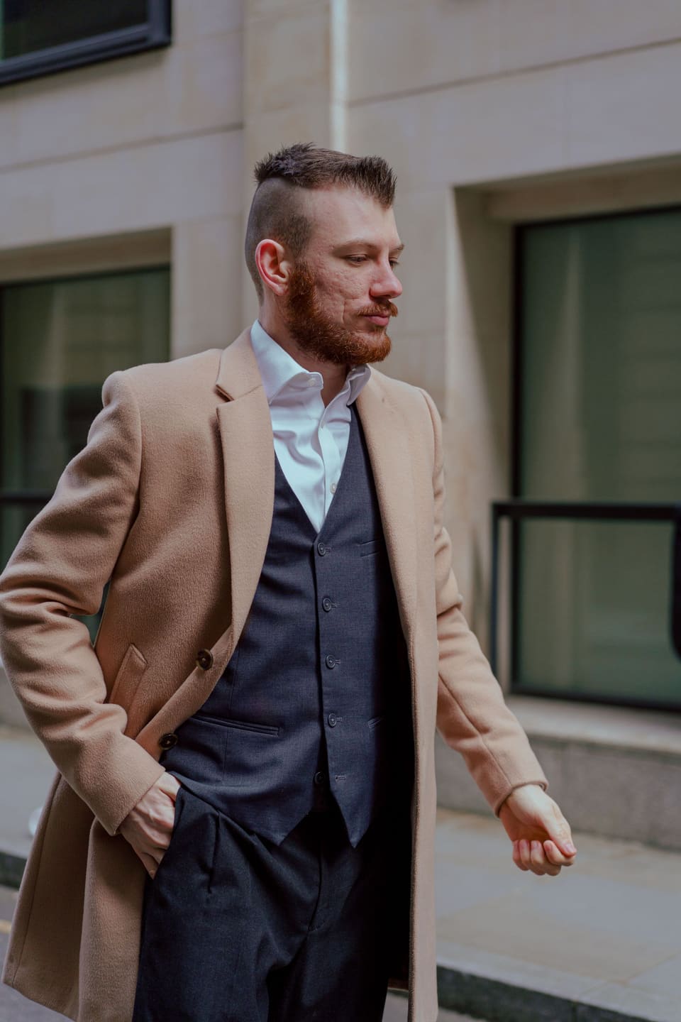 The sharp suit: Bearded man in a camel coat and suit walking confidently in an urban setting.