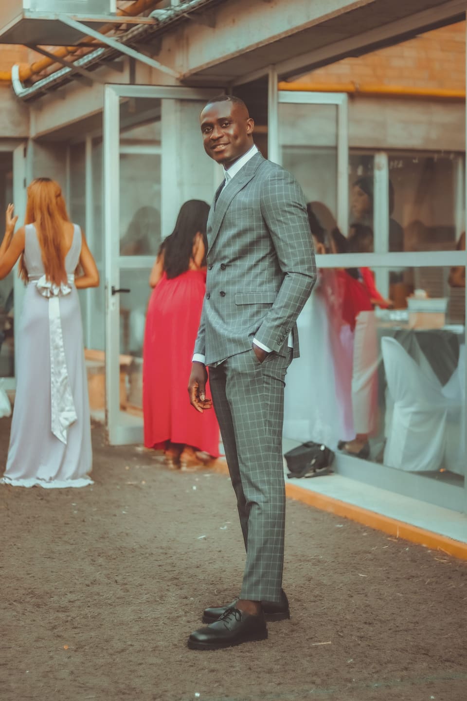 Stylish man in a grey checkered suit posing outdoors at a wedding.