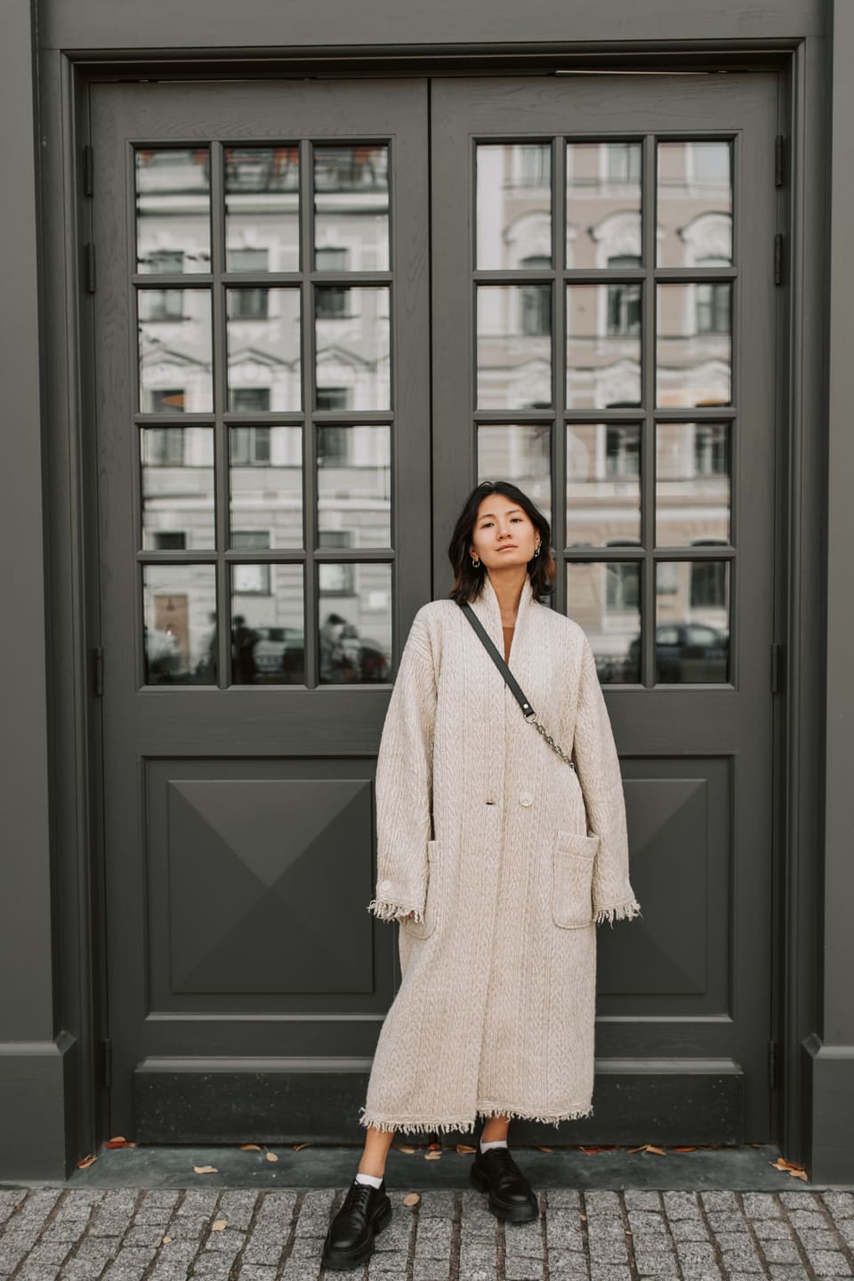 Scandi minimal: Stylish woman in a trench coat standing confidently against a dark door.